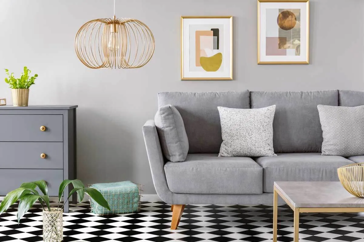 A freshly decorated living room with a grey sofa, framed prints and a gold pendant light